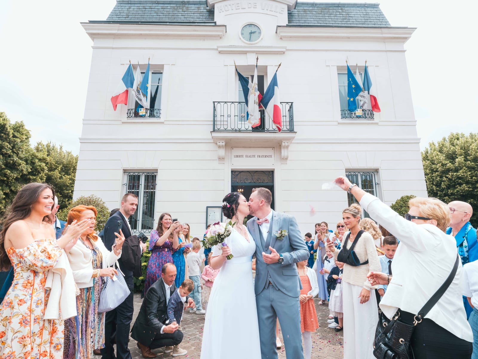Sortie de la mairie d'Auvers-sur-Oise sous une pluie de confettis colorés, invités rassemblés, mariage au Domaine de la Muette, par Jean-Baptiste Argyre (Jaysphotography)