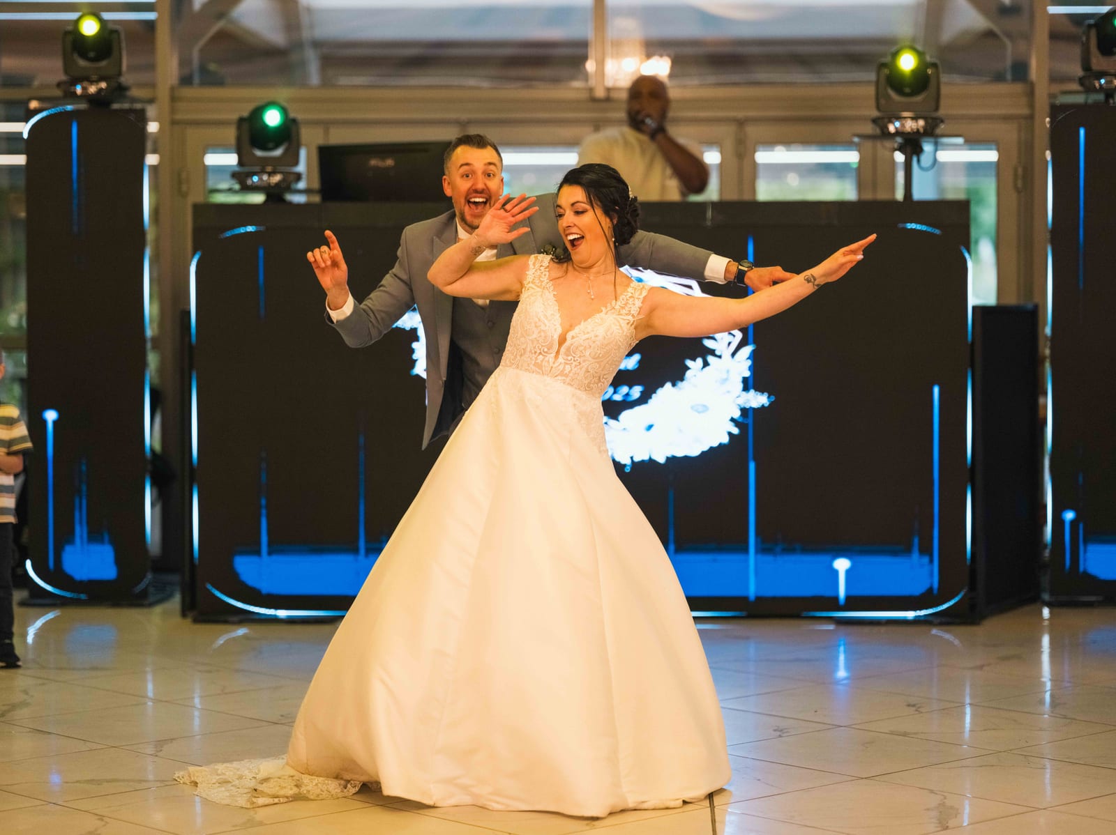 Mélissa entre dans la salle de réception bras levés, DJ en fond sur la piste de danse, mariage au Domaine de la Muette, par Jean-Baptiste Argyre (Jaysphotography)