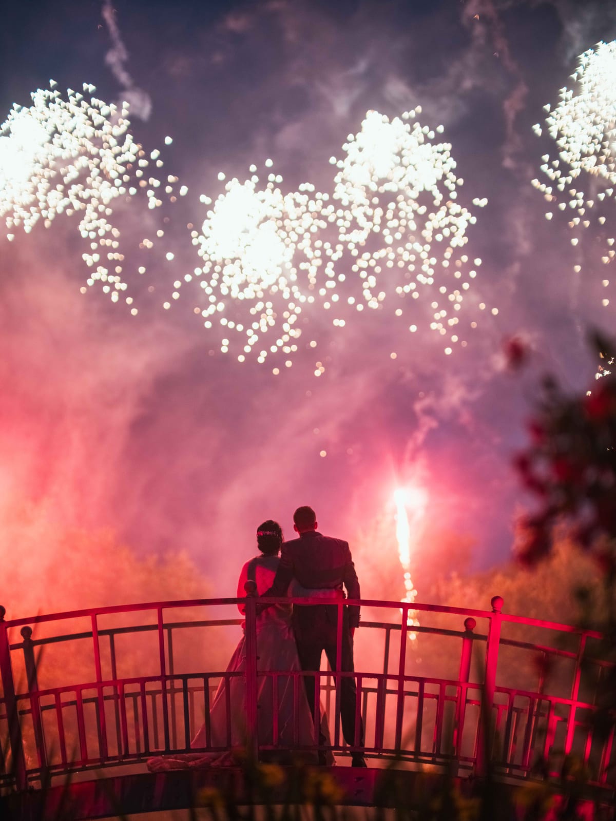 Feu d'artifice rouge et blanc vu depuis la terrasse du domaine, silhouettes de dos, mariage au Domaine de la Muette, par Jean-Baptiste Argyre (Jaysphotography)