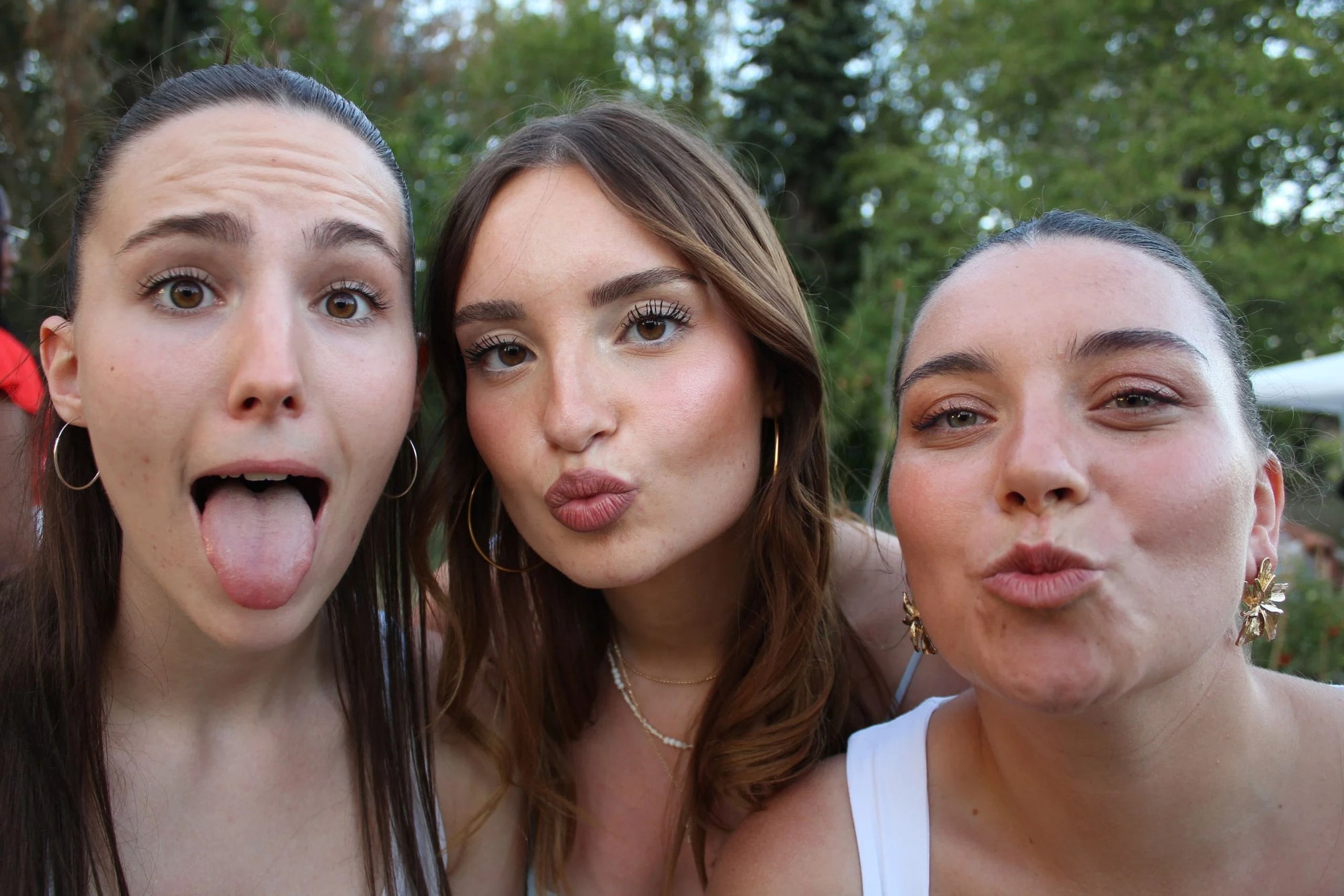 Trois invitées font des grimaces face à la borne, langue tirée et bouche en cœur, arbres du jardin en fond, mariage au Neuilly-en-Thelle (Oise), par Jean-Baptiste Argyre (Jaysphotography)