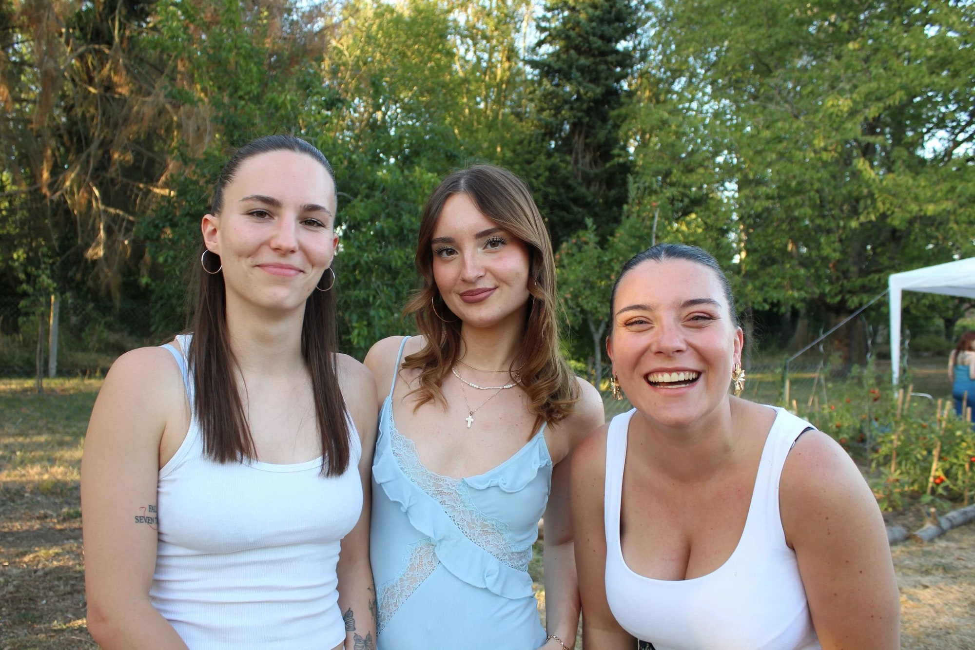 Trois invitées côte à côte dans la lumière dorée de vingt heures, débardeurs blancs et robe bleu ciel, mariage au Neuilly-en-Thelle (Oise), par Jean-Baptiste Argyre (Jaysphotography)