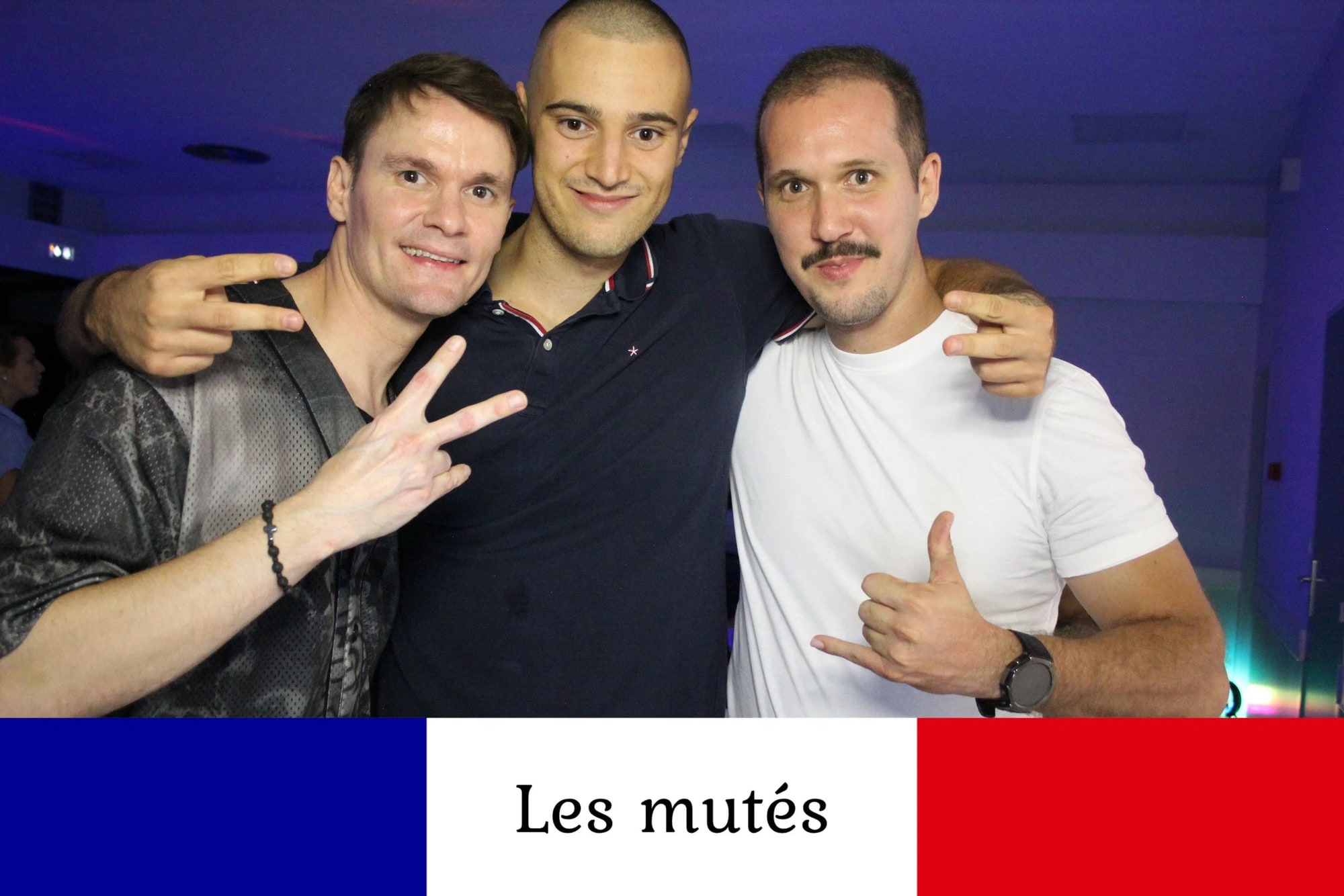 Trois hommes bras dessus bras dessous font des signes de la main devant l'objectif, tirage au bandeau bleu blanc rouge, mariage à la Salle des fêtes de Saint-Sauveur (Oise), par Jean-Baptiste Argyre (Jaysphotography)