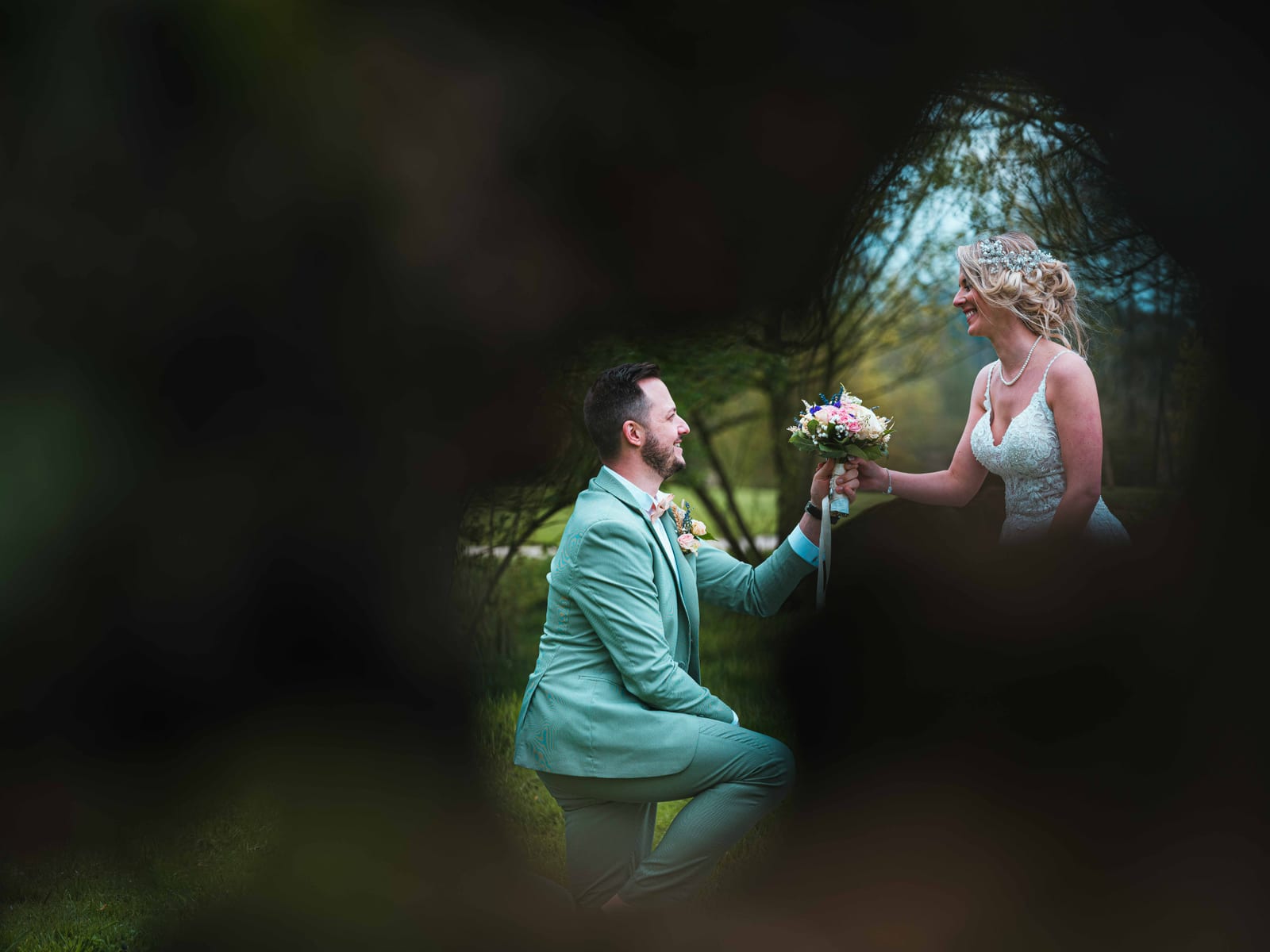 Romain à genoux passant la bague à Julie lors de la cérémonie laïque extérieure, arche fleurie, Domaine des Saules, mariage au Domaine des Saules, par Jean-Baptiste Argyre (Jaysphotography)