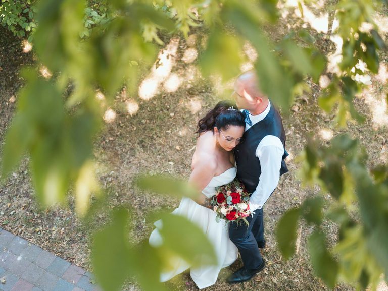 Sarah blottie contre Anthony vue en plongée à travers les feuilles, bouquet rouge et crème