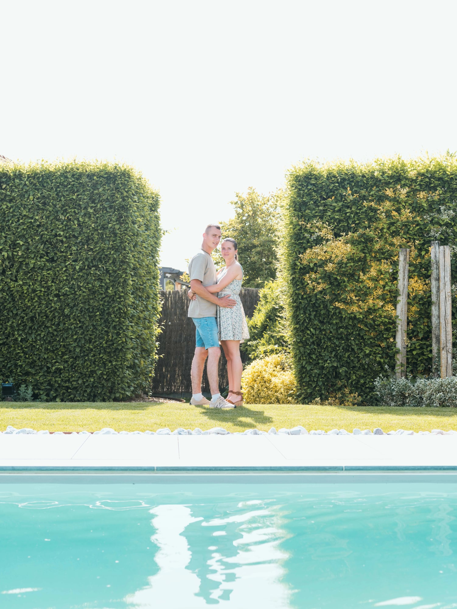 Amélie et Guillaume enlacés entre les haies du jardin familial, piscine au premier plan, mariage au Le jardin de la famille, avec piscine (Oise), par Jean-Baptiste Argyre (Jaysphotography)