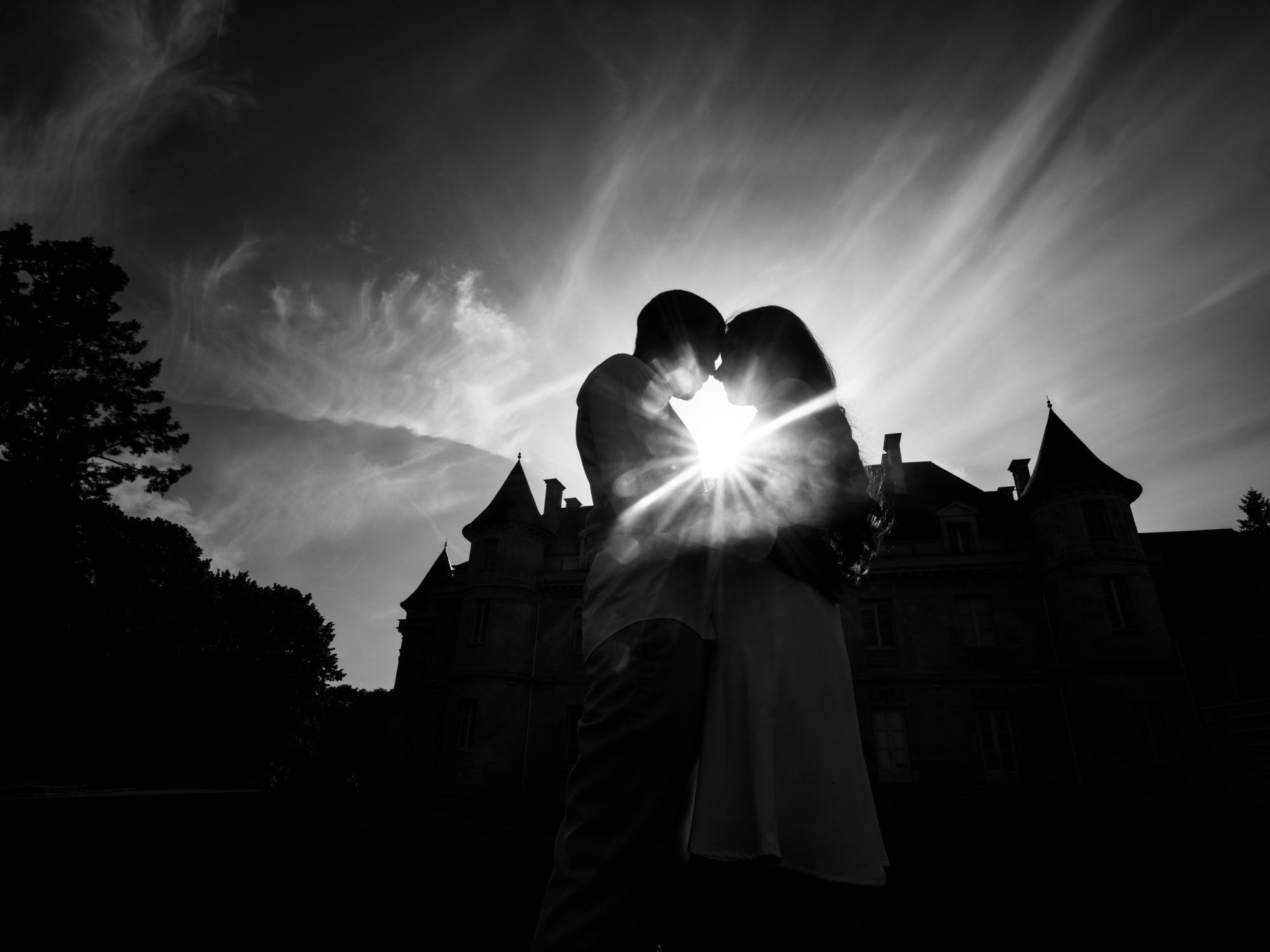 Silhouettes du couple en noir et blanc, soleil en étoile derrière le château, mariage au Château de Lamorlaye, par Jean-Baptiste Argyre (Jaysphotography)